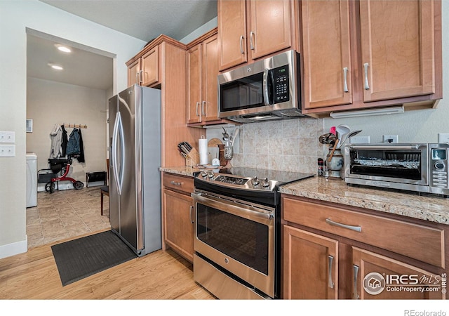 kitchen with light stone countertops, brown cabinets, washer / dryer, and appliances with stainless steel finishes