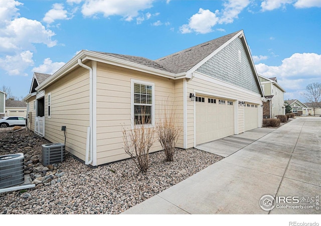 view of home's exterior with roof with shingles, cooling unit, an attached garage, and concrete driveway