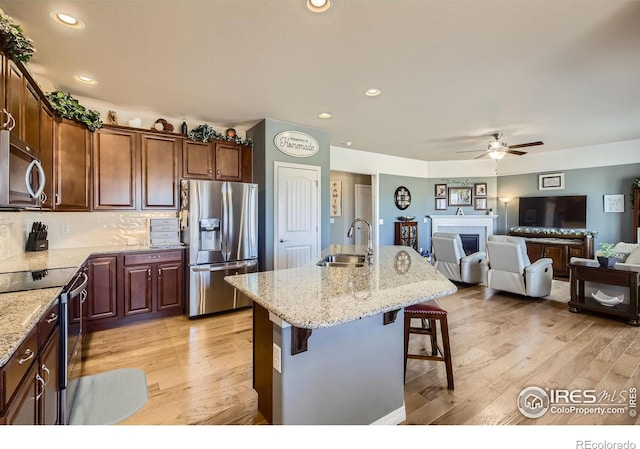 5460 Homeward Dr, Timnath, CO 80547 - kitchen with appliances with stainless steel finishes, a sink, a ceiling fan, a breakfast bar, and a fireplace