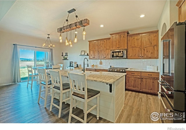 27857 Hopi Trl, Loveland, CO 80534 - kitchen with light wood finished floors, stainless steel appliances, backsplash, a kitchen bar, and brown cabinetry