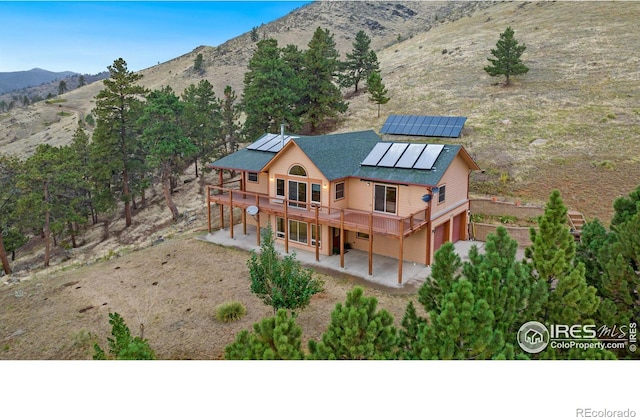 10435 Roan Mountain Rd, Loveland, CO 80538 - back of property featuring a deck with mountain view, roof mounted solar panels, a patio, a garage, and driveway