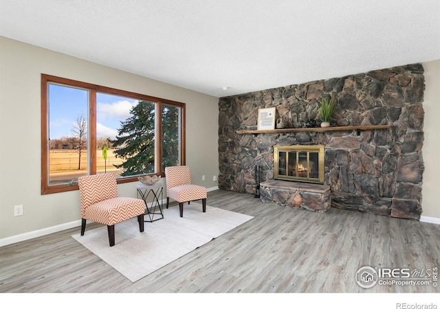 sitting room with a stone fireplace, baseboards, and wood finished floors