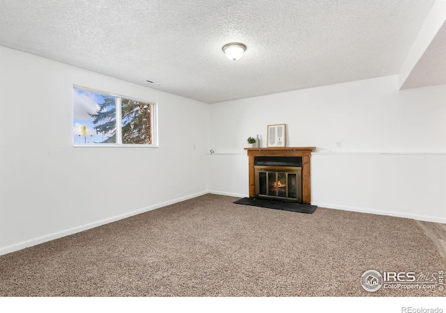 unfurnished living room with baseboards, a textured ceiling, a glass covered fireplace, and carpet