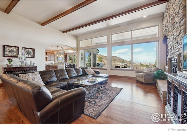 living area with arched walkways, beamed ceiling, a notable chandelier, and wood finished floors