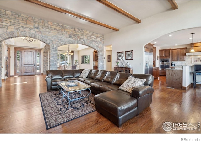 living area with a chandelier, arched walkways, dark wood-type flooring, and beam ceiling