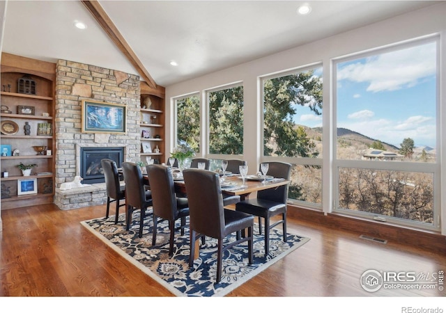 dining area with a stone fireplace, visible vents, vaulted ceiling with beams, and wood finished floors