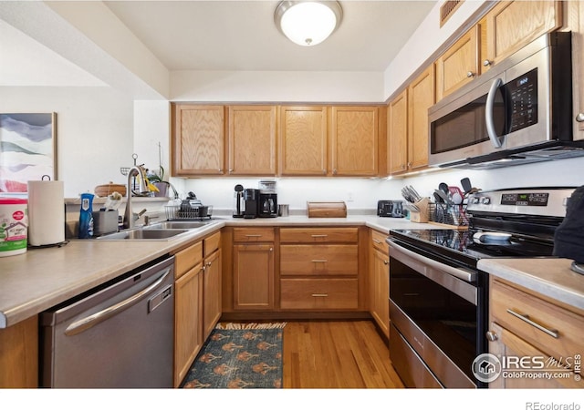 kitchen with light countertops, a sink, stainless steel appliances, and light wood finished floors