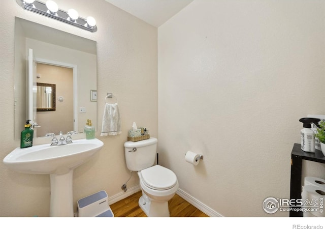 half bathroom with toilet, wood finished floors, and baseboards