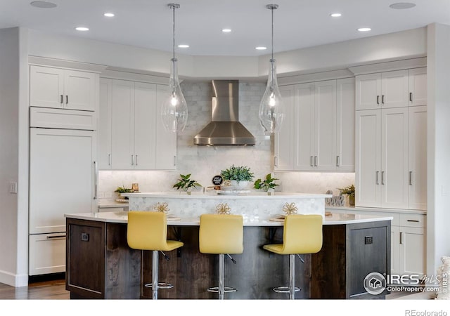 kitchen featuring white cabinetry, paneled refrigerator, and wall chimney exhaust hood