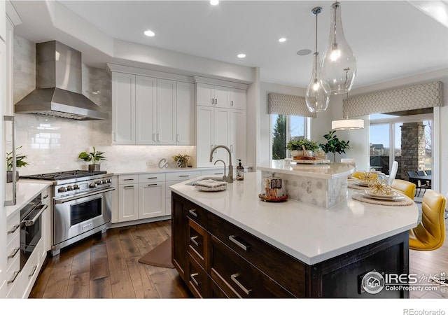 kitchen with dark wood finished floors, wall chimney exhaust hood, light countertops, and appliances with stainless steel finishes