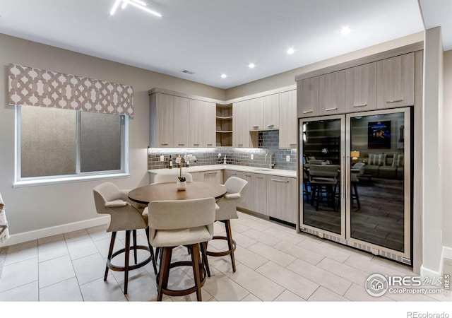 kitchen with light countertops, a sink, open shelves, beverage cooler, and backsplash