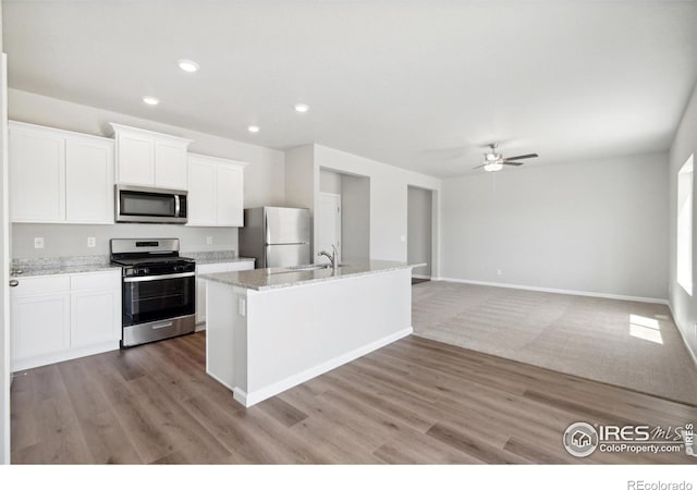 kitchen with an island with sink, a ceiling fan, appliances with stainless steel finishes, white cabinets, and light wood-style floors