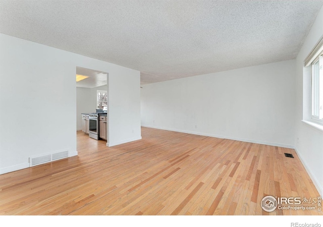 spare room featuring light wood-style flooring, a textured ceiling, baseboards, and visible vents