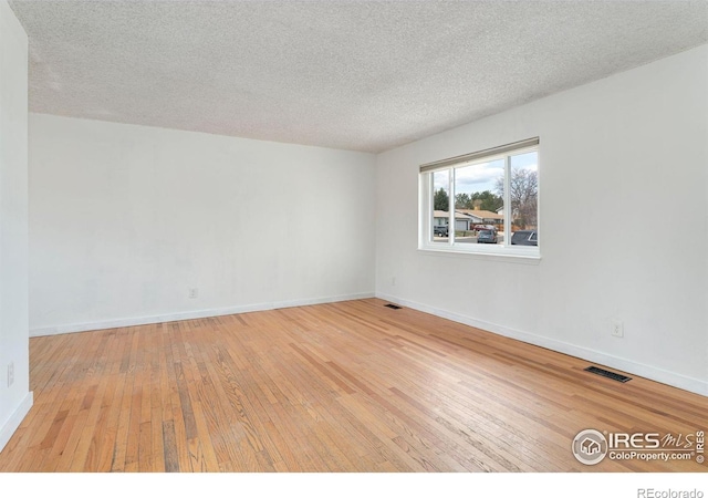 empty room with baseboards, a textured ceiling, wood-type flooring, and visible vents