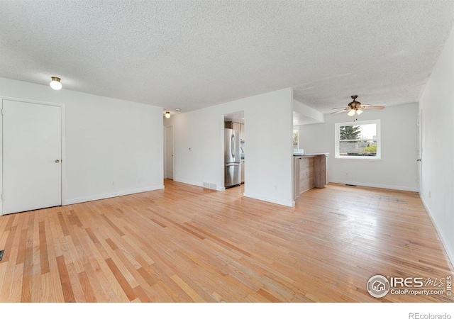 unfurnished living room with a ceiling fan, baseboards, light wood-type flooring, and a textured ceiling