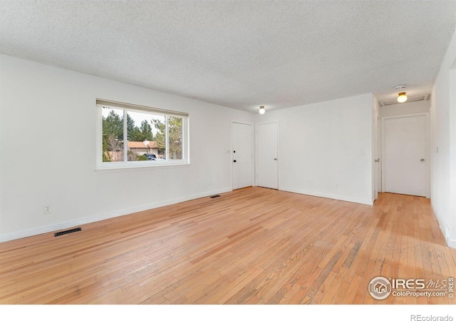 unfurnished room with light wood-type flooring, baseboards, visible vents, and a textured ceiling