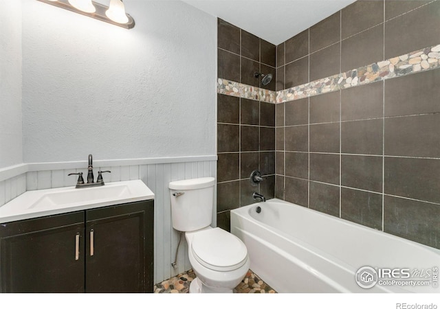 bathroom featuring shower / bathtub combination, vanity, a wainscoted wall, toilet, and a textured wall