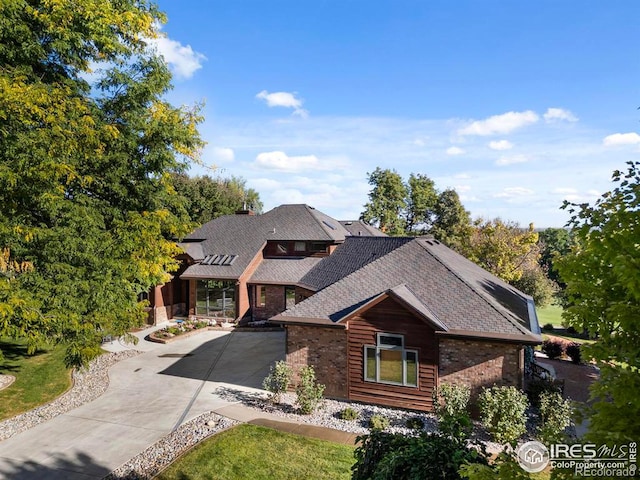 view of front of home featuring brick siding, driveway, and roof with shingles