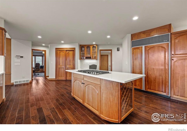 kitchen featuring stainless steel gas cooktop, a center island, paneled built in fridge, visible vents, and glass insert cabinets