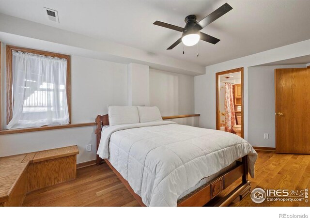 bedroom with baseboards, connected bathroom, light wood finished floors, visible vents, and a ceiling fan