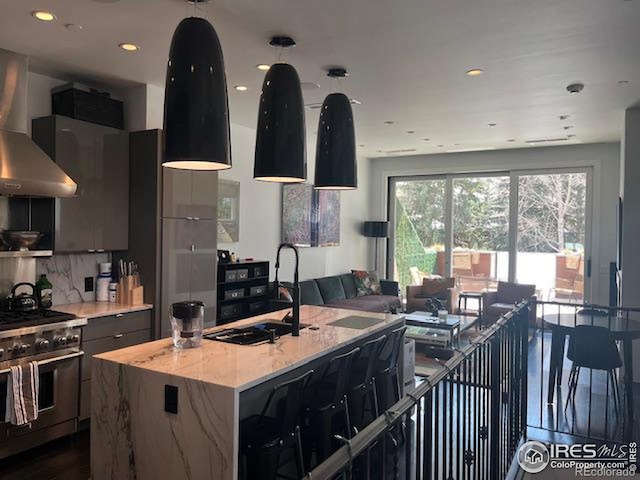 100 E Cooper Ave E Unit 7, Aspen, CO 81611 - kitchen featuring high end stainless steel range, a kitchen island with sink, a sink, open floor plan, and wall chimney range hood