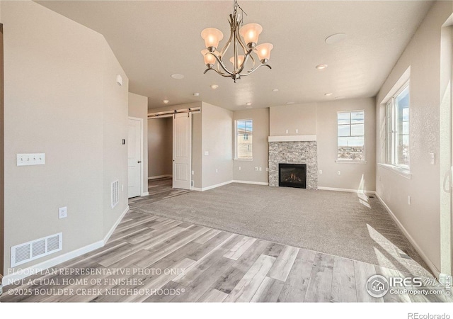 2387 Bristol St, Superior, CO 80027 - unfurnished living room with a barn door, light wood-style flooring, baseboards, a stone fireplace, and a chandelier