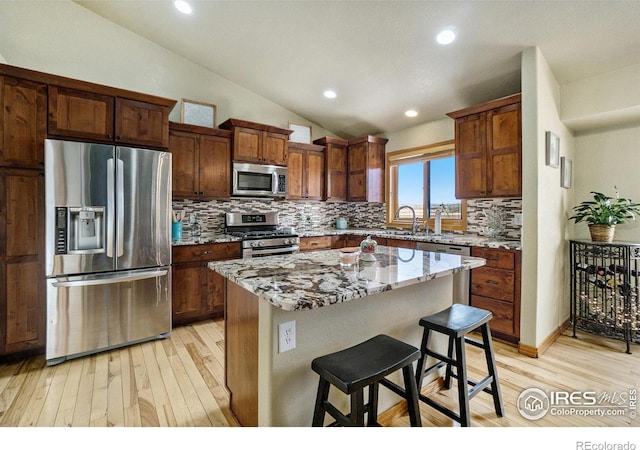 7889 Antelope Ct, Wellington, CO 80549 - kitchen featuring decorative backsplash, appliances with stainless steel finishes, lofted ceiling, light wood-type flooring, and a breakfast bar area