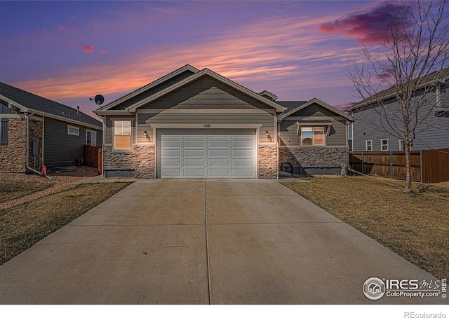 1108 Osprey Way, Wiggins, CO 80654 - view of front facade featuring stone siding, fence, an attached garage, concrete driveway, and a front lawn