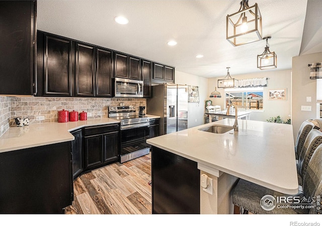 1108 Osprey Way, Wiggins, CO 80654 - kitchen featuring light countertops, light wood finished floors, stainless steel appliances, tasteful backsplash, and dark cabinets