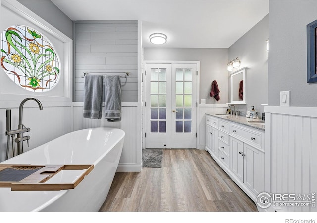 6850 Frying Pan Rd, Boulder, CO 80301 - bathroom featuring french doors, wood finished floors, double vanity, a freestanding bath, and a wainscoted wall