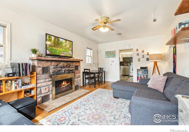 living area with visible vents, ceiling fan, wood finished floors, and a stone fireplace