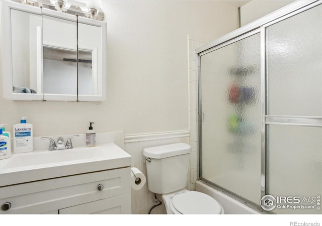 bathroom featuring vanity, toilet, bath / shower combo with glass door, and wainscoting