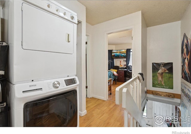 laundry area featuring a textured ceiling, light wood-style flooring, stacked washer and clothes dryer, laundry area, and baseboards