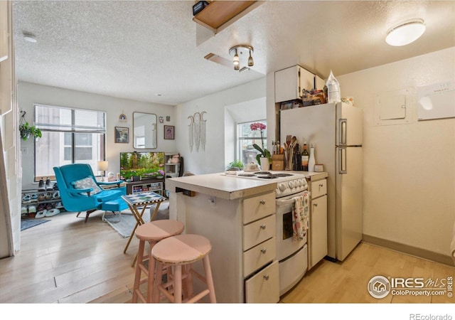 kitchen featuring a textured ceiling, light wood-style flooring, light countertops, a peninsula, and white appliances