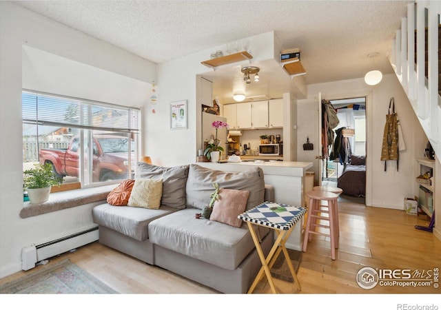 living room with a textured ceiling, a baseboard heating unit, and light wood-type flooring