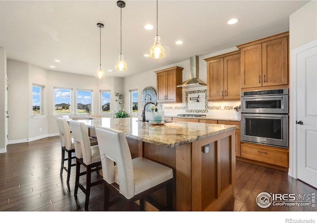 kitchen with a sink, dark wood finished floors, brown cabinetry, wall chimney exhaust hood, and backsplash