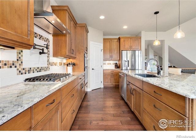 kitchen with brown cabinets, appliances with stainless steel finishes, a sink, wall chimney exhaust hood, and dark wood-type flooring