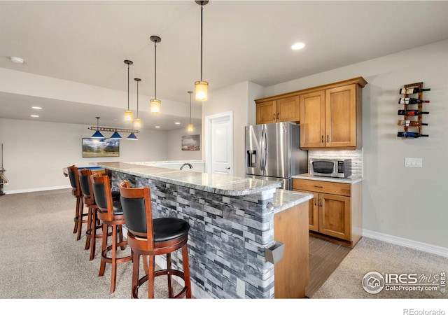 kitchen with decorative light fixtures, baseboards, appliances with stainless steel finishes, and an island with sink