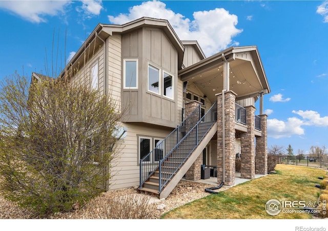 rear view of house with stairs, board and batten siding, a yard, and stone siding
