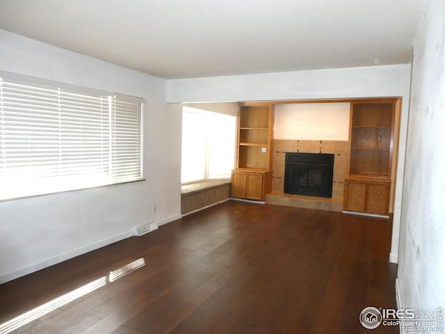 unfurnished living room with dark wood-type flooring, visible vents, baseboards, and a tile fireplace