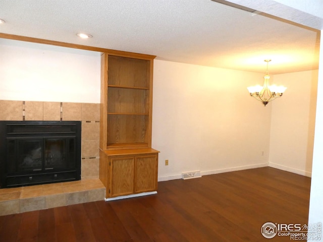 unfurnished living room with visible vents, wood finished floors, a tiled fireplace, baseboards, and a notable chandelier