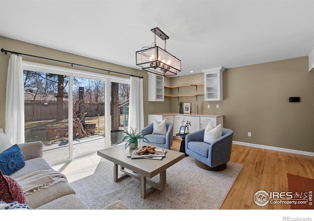 living area featuring baseboards, light wood-style flooring, and a notable chandelier