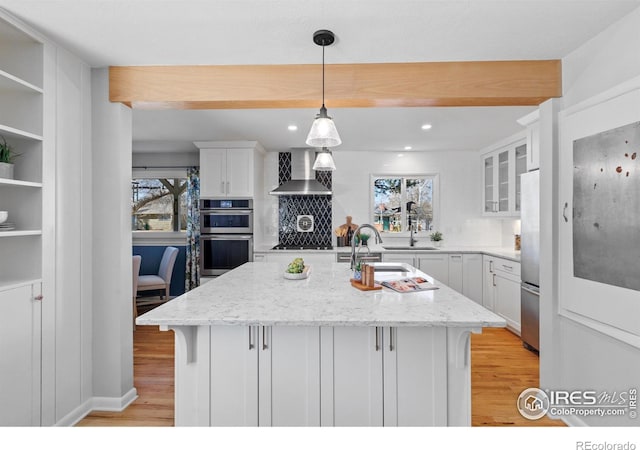 kitchen featuring wall chimney exhaust hood, light wood-style flooring, appliances with stainless steel finishes, and white cabinets