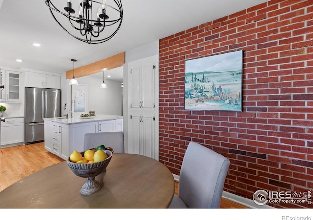 dining area with light wood finished floors, recessed lighting, a notable chandelier, and brick wall