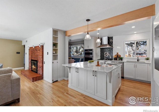 kitchen featuring wall chimney range hood, a fireplace, light wood-type flooring, and double oven