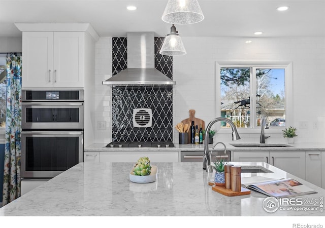 kitchen with tasteful backsplash, a sink, white cabinets, appliances with stainless steel finishes, and wall chimney exhaust hood