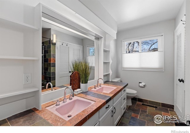 full bathroom with baseboards, double vanity, a sink, and stone tile flooring