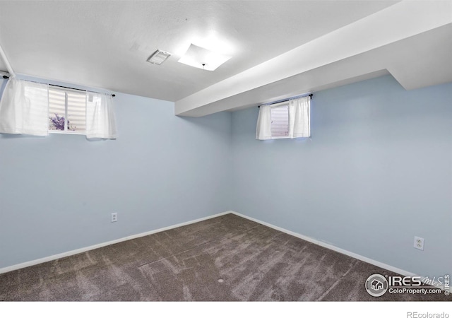 below grade area featuring baseboards, dark colored carpet, and visible vents