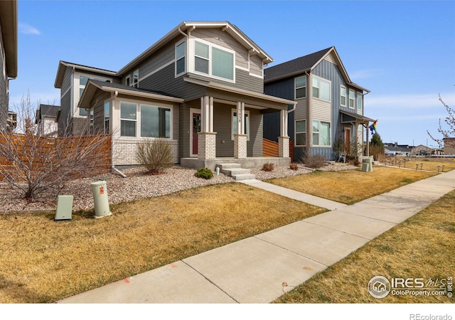 craftsman inspired home with covered porch, a front lawn, and brick siding