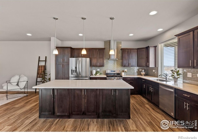 kitchen with wall chimney exhaust hood, stainless steel appliances, dark brown cabinetry, a sink, and a center island